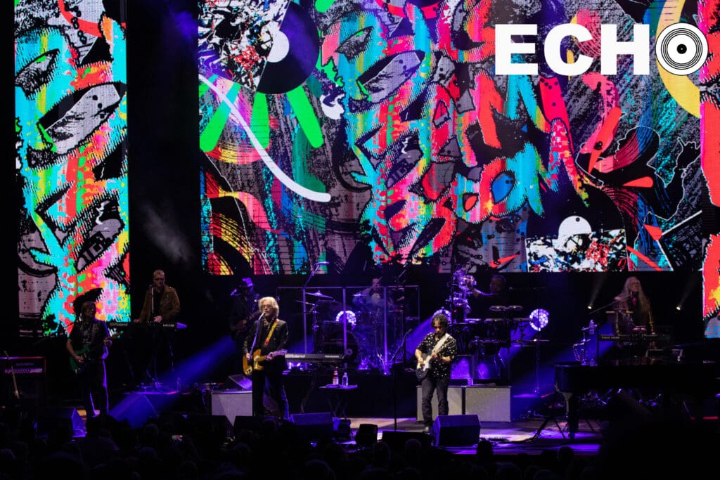 Hall, Oates, and the band play in front of colorful backdrop